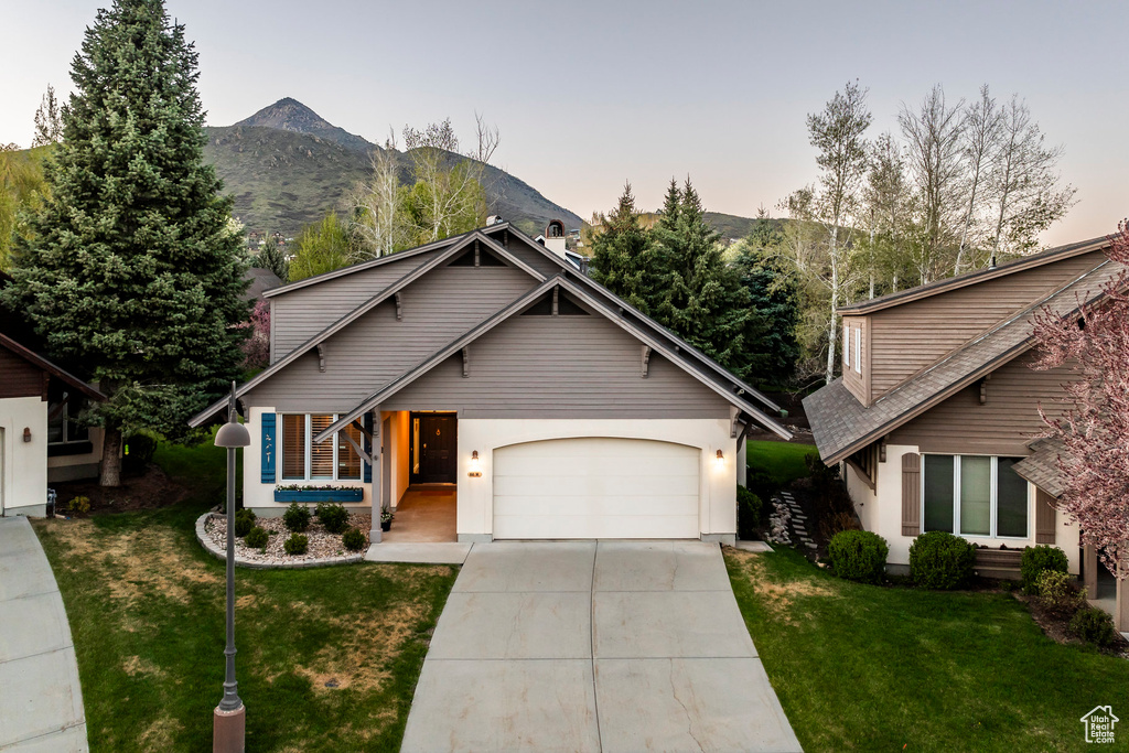 View of front of house with an attached garage, concrete driveway, a front yard, and a mountain view