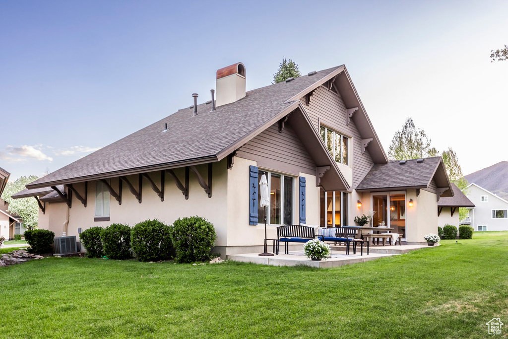 Rear view of house featuring a patio area, a shingled roof, a chimney, a yard, and stucco siding