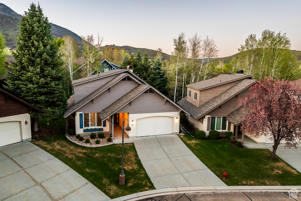 Traditional-style house with concrete driveway, a lawn, a garage, a mountain view, and roof with shingles