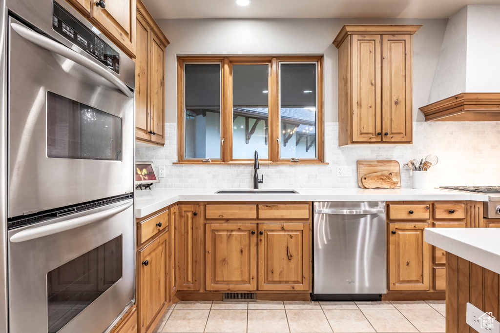 Kitchen featuring appliances with stainless steel finishes, wall chimney range hood, a sink, light countertops, and backsplash