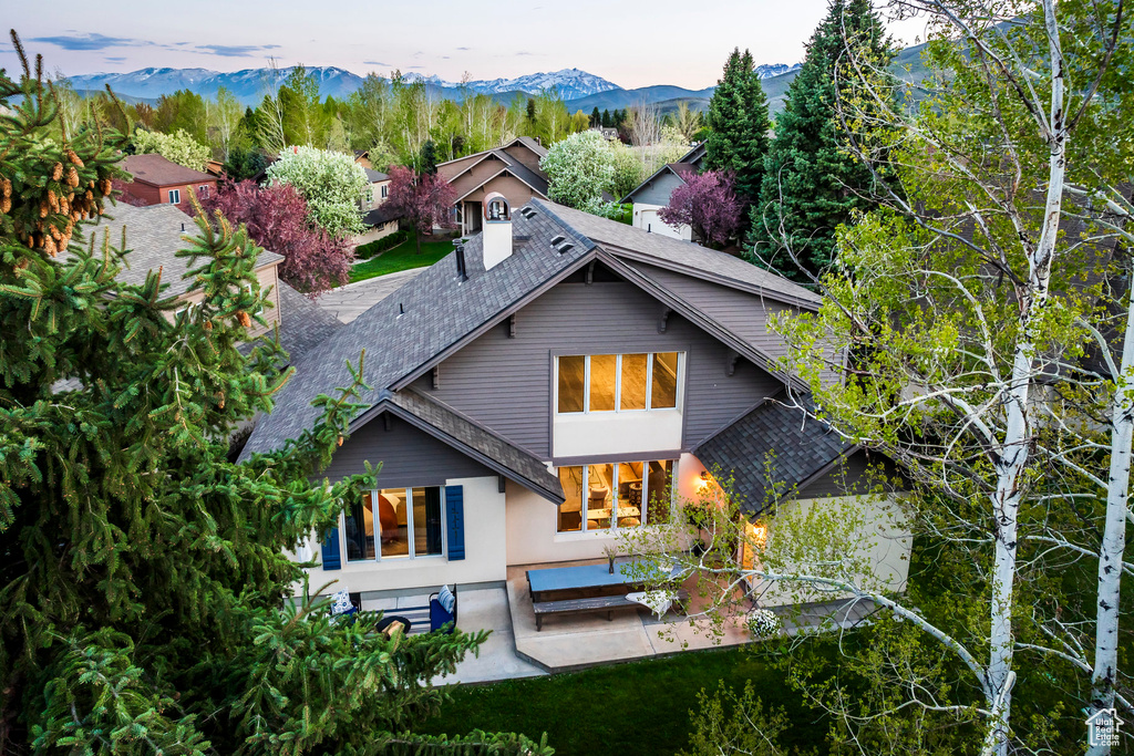 Rear view of property featuring a shingled roof, a patio, a mountain view, and stucco siding