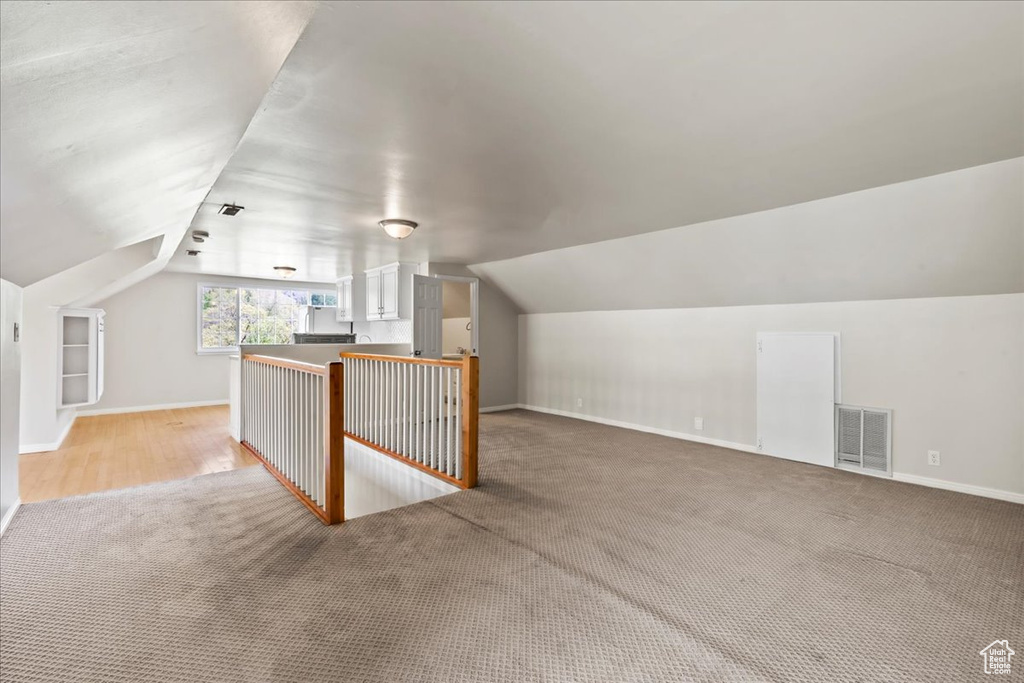 Bonus room featuring light carpet, lofted ceiling, and baseboards