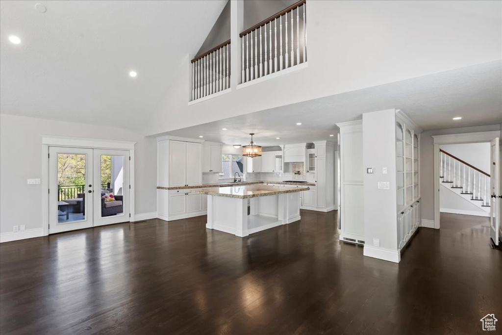 Unfurnished living room with french doors, stairway, high vaulted ceiling, dark wood finished floors, and baseboards