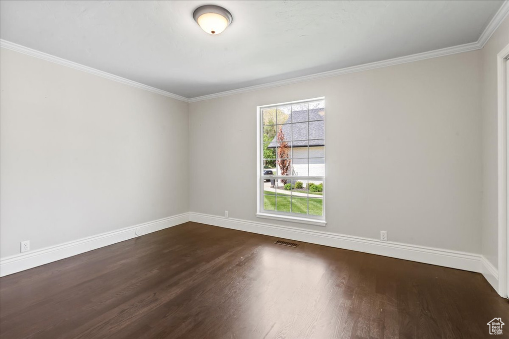 Empty room with dark wood-style flooring, baseboards, and ornamental molding