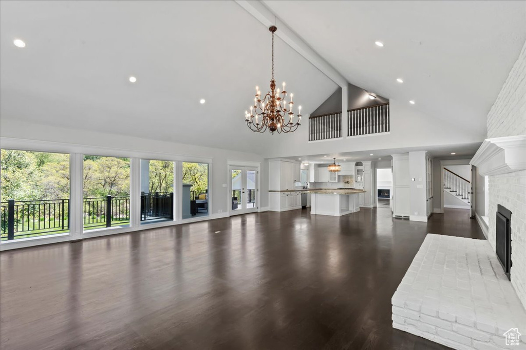 Unfurnished living room featuring a chandelier, high vaulted ceiling, plenty of natural light, recessed lighting, and dark wood-style flooring