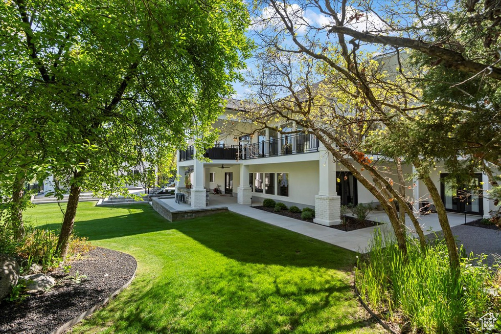 Rear view of house featuring a balcony, stucco siding, a lawn, and a patio area