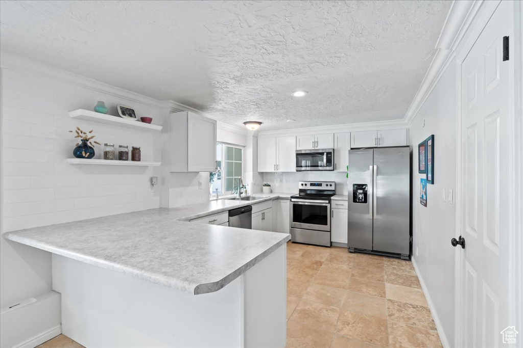 Kitchen with stainless steel appliances, a peninsula, a sink, light countertops, and white cabinetry