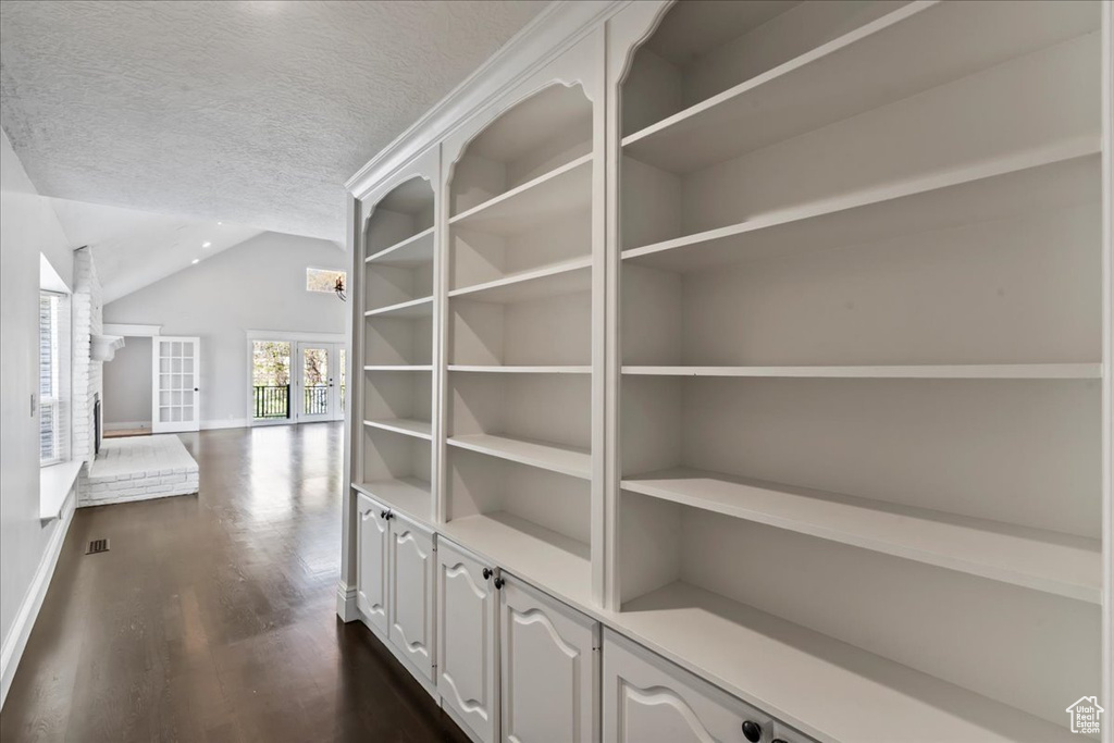 Corridor with lofted ceiling, dark wood-type flooring, baseboards, a textured ceiling, and french doors