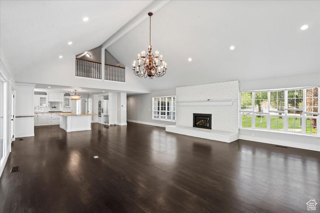 Unfurnished living room featuring high vaulted ceiling, a fireplace, a chandelier, baseboards, and dark wood-style floors