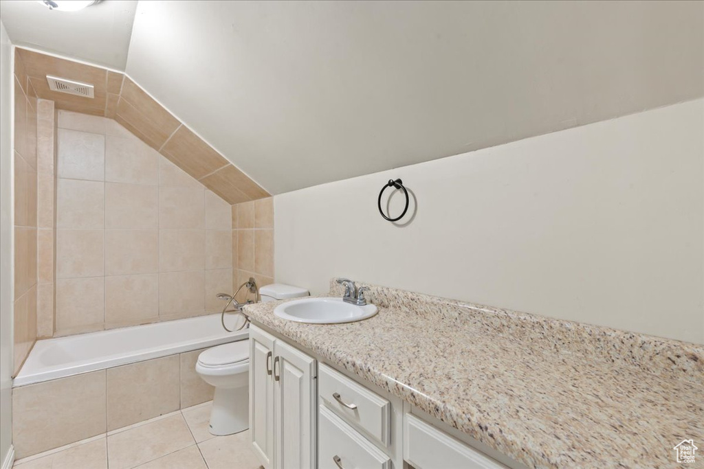 Full bathroom with tile patterned floors, tiled bath, toilet, vanity, and lofted ceiling
