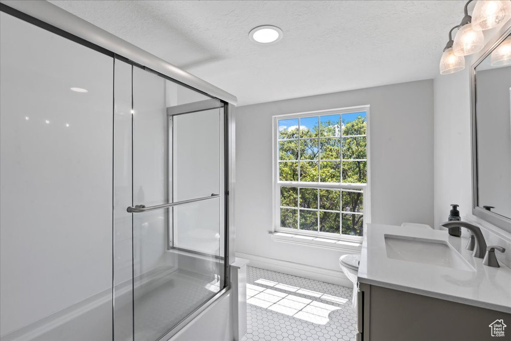 Bathroom with an enclosed shower, vanity, toilet, and tile patterned flooring
