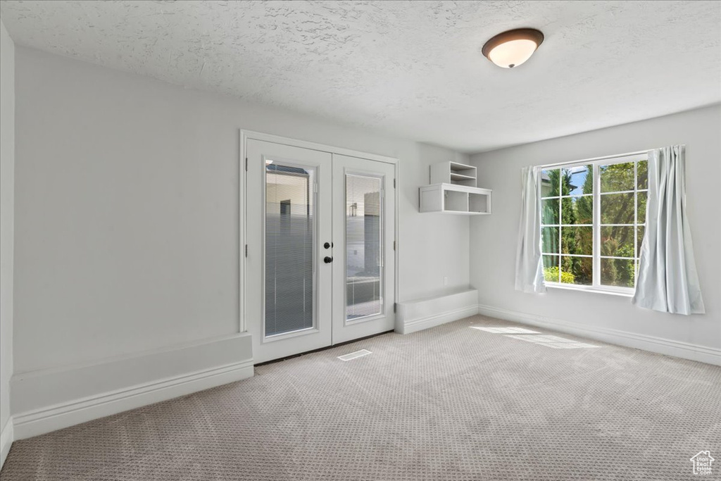Carpeted spare room with french doors, baseboards, and a textured ceiling