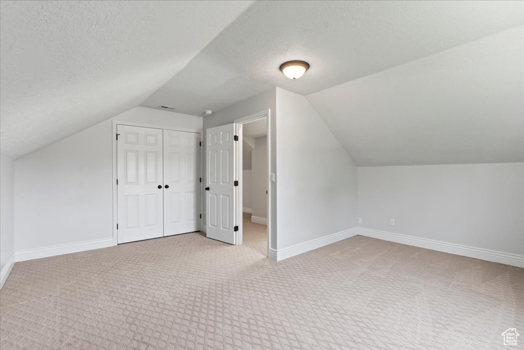 Additional living space with vaulted ceiling, light carpet, baseboards, and a textured ceiling