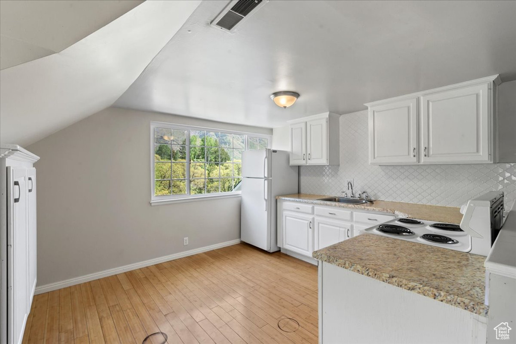 Kitchen featuring white appliances, a sink, decorative backsplash, light countertops, and vaulted ceiling