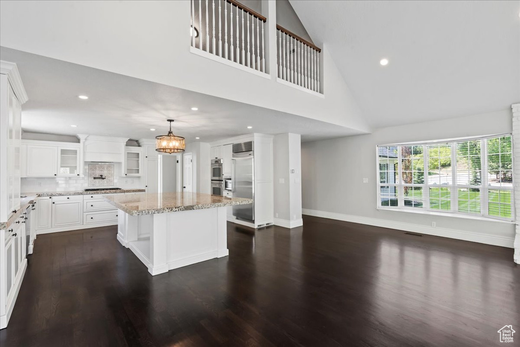 Kitchen with appliances with stainless steel finishes, a center island, glass insert cabinets, light stone counters, and high vaulted ceiling