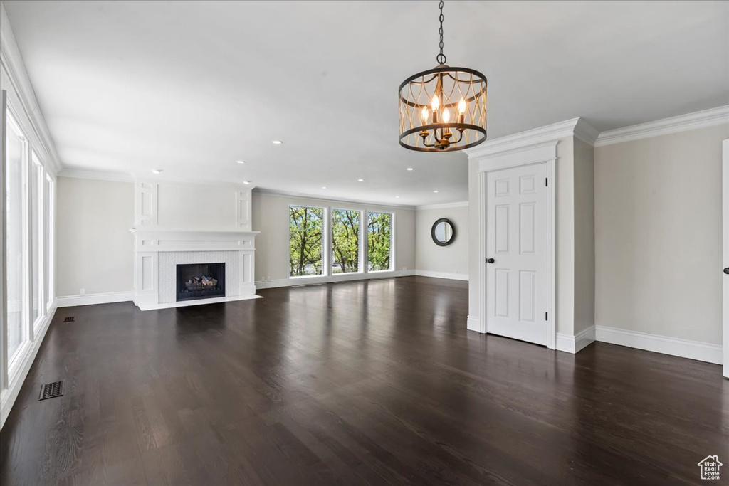 Unfurnished living room with a chandelier, baseboards, dark wood-style flooring, recessed lighting, and ornamental molding