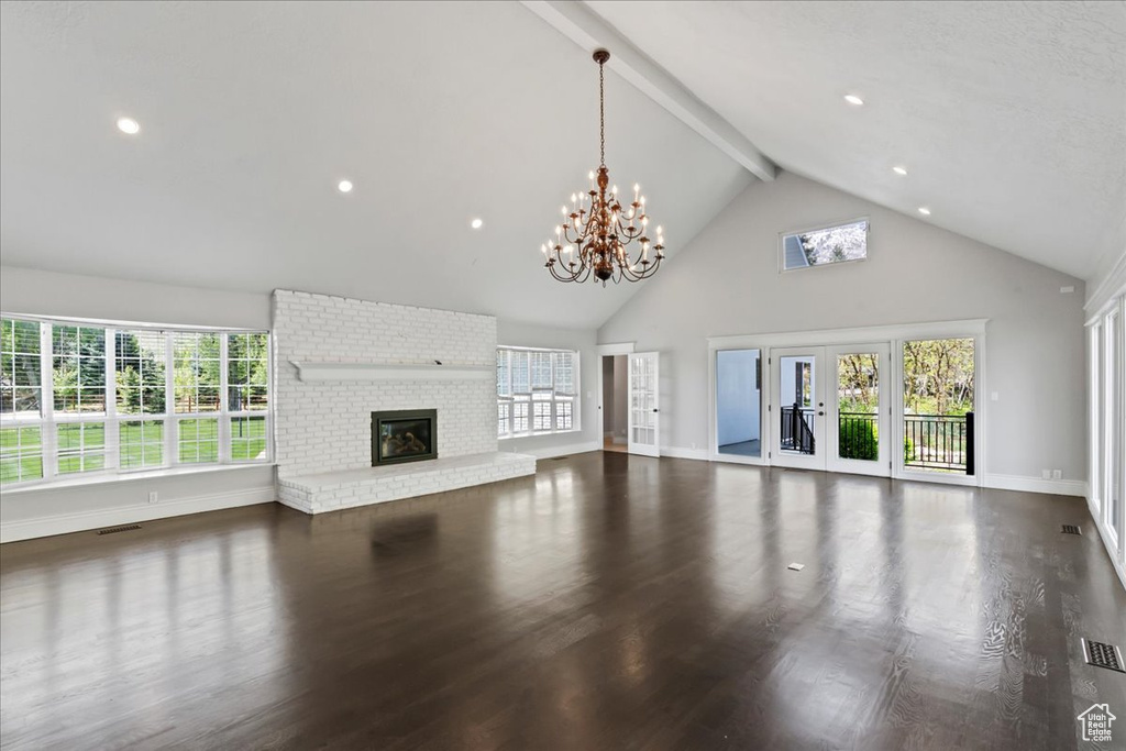 Unfurnished living room with high vaulted ceiling, beamed ceiling, a brick fireplace, a chandelier, and baseboards