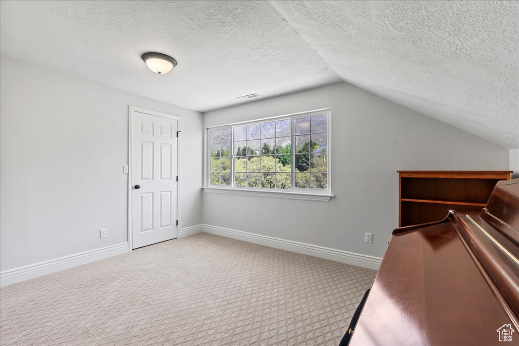 Unfurnished bedroom with a textured ceiling, carpet flooring, lofted ceiling, and baseboards