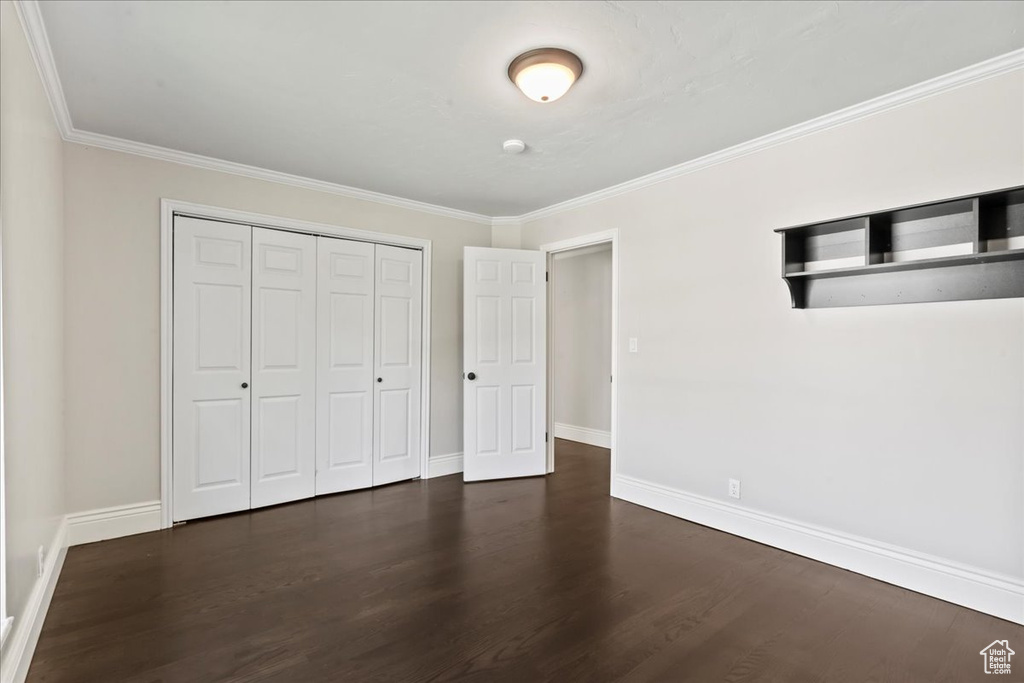 Unfurnished bedroom with dark wood-type flooring, baseboards, crown molding, and a closet
