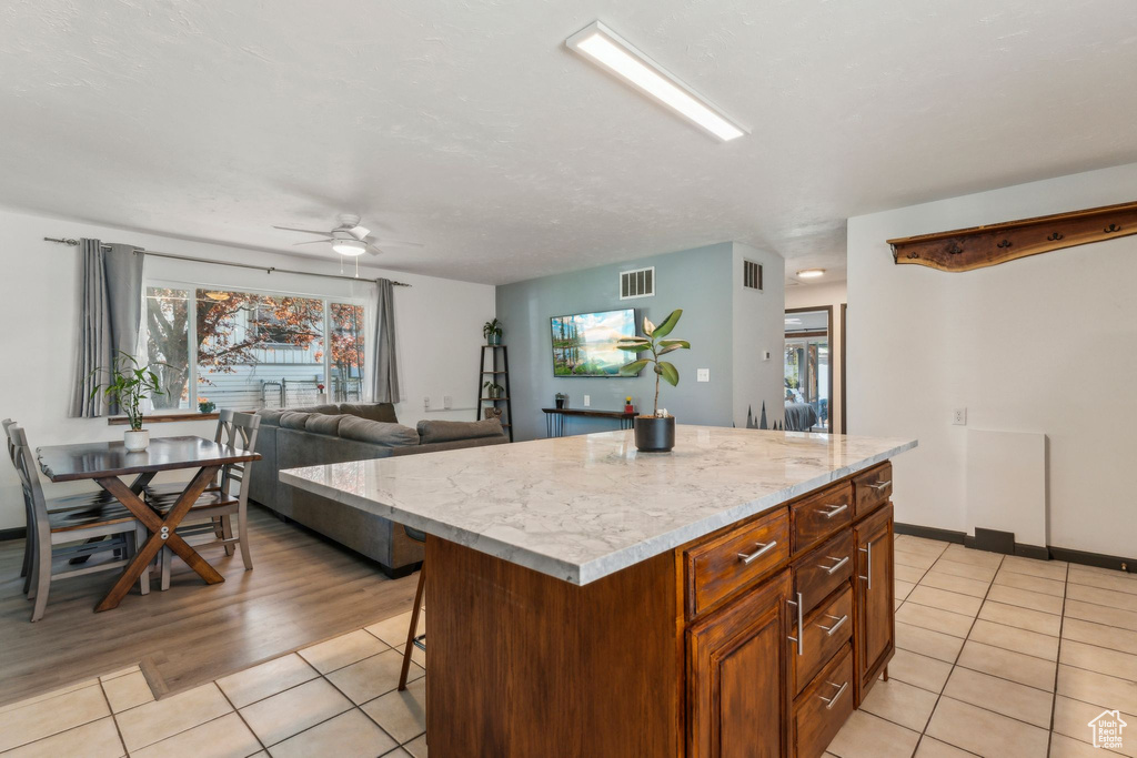 Kitchen featuring light tile patterned flooring, a ceiling fan, a kitchen island, and light stone counters