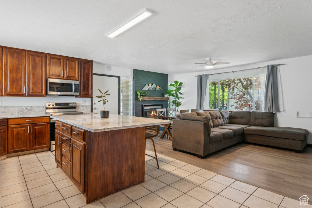 Kitchen with appliances with stainless steel finishes, a kitchen breakfast bar, a fireplace, a ceiling fan, and open floor plan