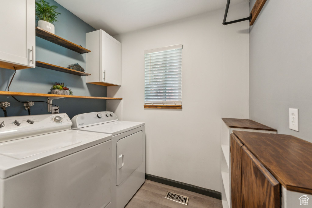Washroom featuring washer and clothes dryer, light wood-style floors, cabinet space, and baseboards