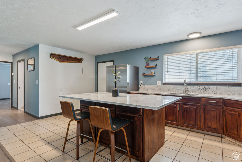 Kitchen featuring a sink, freestanding refrigerator, a kitchen bar, a kitchen island, and light stone countertops