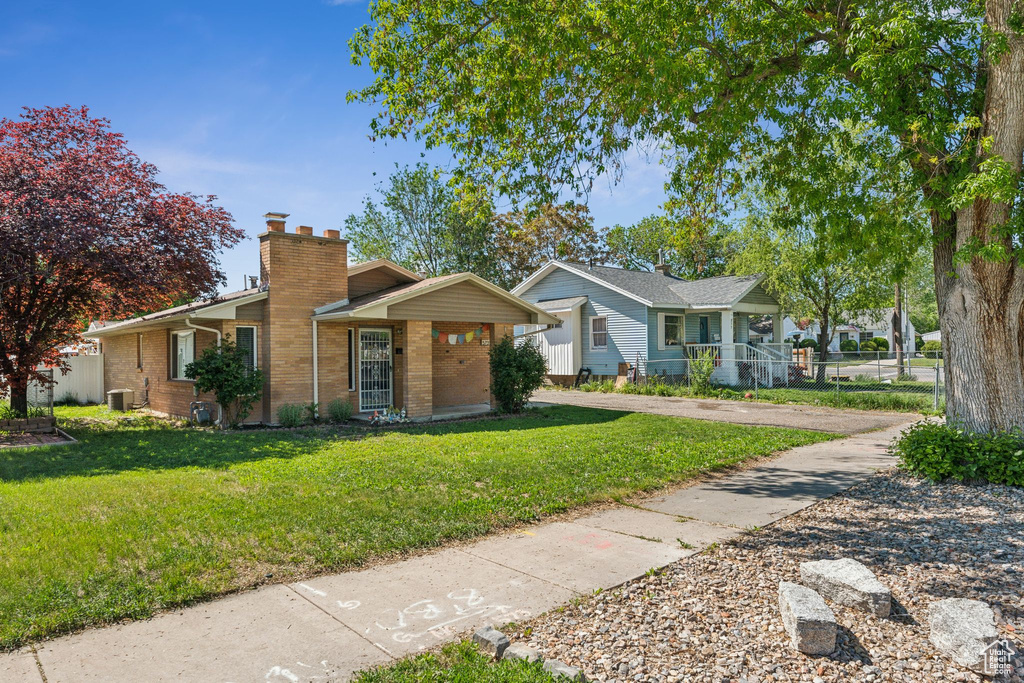 View of front of property with brick siding, a front lawn, a chimney, central air condition unit, and a porch