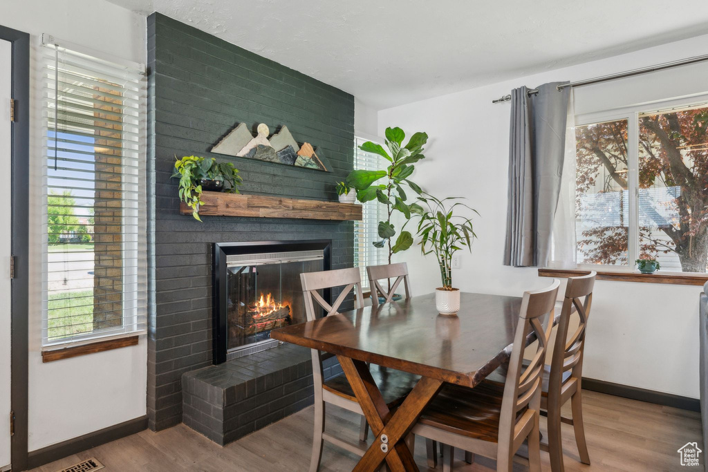 Dining room featuring a brick fireplace, wood finished floors, healthy amount of natural light, and baseboards