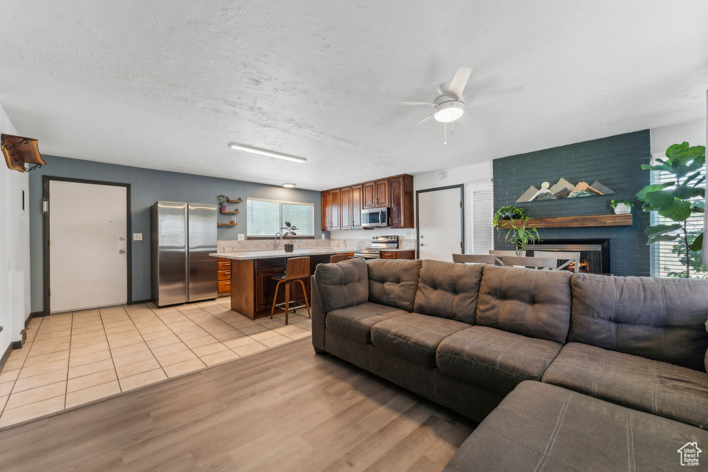 Living area with ceiling fan, light wood finished floors, and a brick fireplace