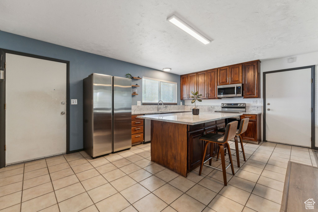 Kitchen featuring stainless steel appliances, light countertops, a breakfast bar area, a kitchen island, and light tile patterned floors