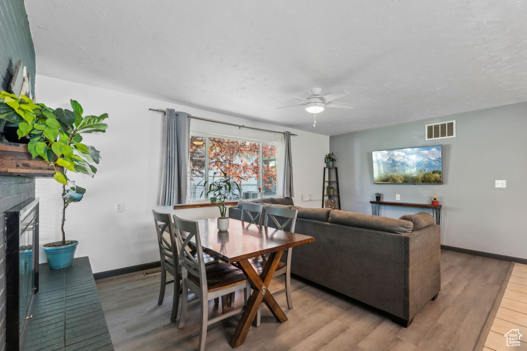 Dining space featuring light wood finished floors, a ceiling fan, a brick fireplace, and baseboards