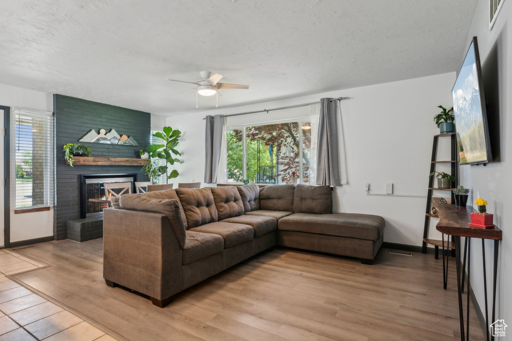 Living area with a ceiling fan, a fireplace, light wood finished floors, a textured ceiling, and baseboards