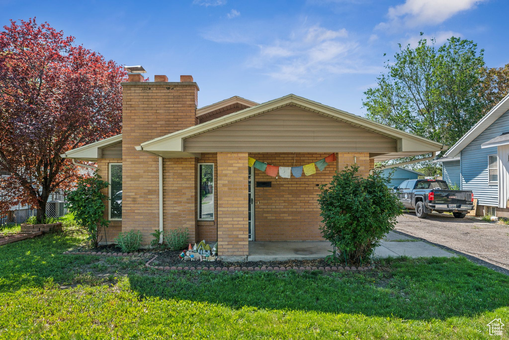 View of front of property featuring brick siding, a front lawn, a chimney, and asphalt driveway
