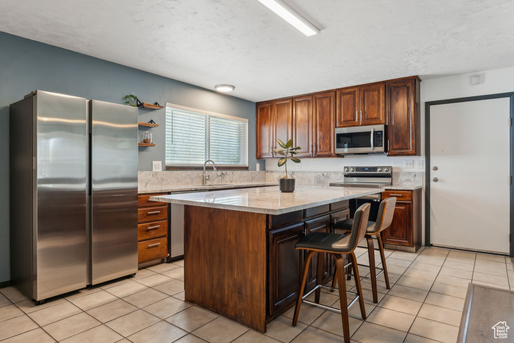 Kitchen with appliances with stainless steel finishes, a kitchen island, a kitchen breakfast bar, light tile patterned flooring, and light stone countertops