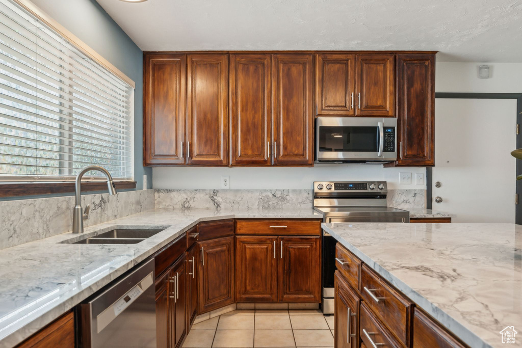 Kitchen featuring stainless steel appliances, a sink, light stone counters, and light tile patterned flooring