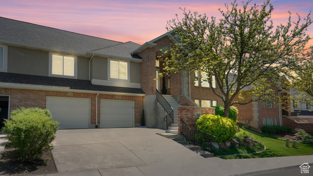 Multi unit property with concrete driveway, a garage, stairway, and brick siding