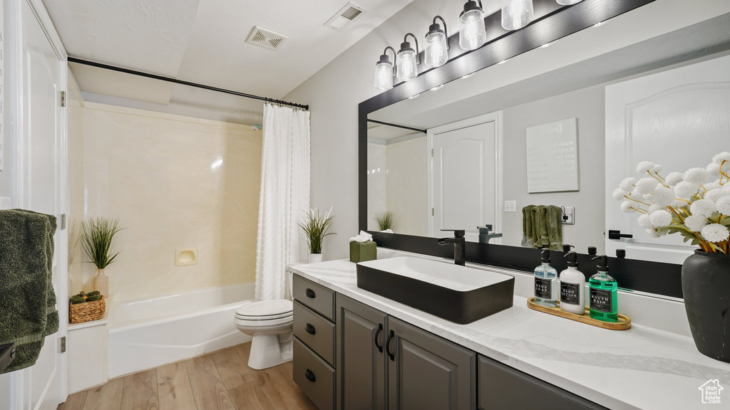 Bathroom featuring toilet, wood finished floors, vanity, and shower / bath combo with shower curtain