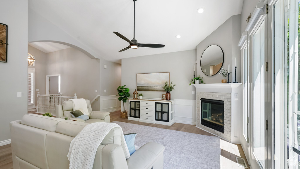 Living room featuring ceiling fan, wood finished floors, arched walkways, wainscoting, and a brick fireplace