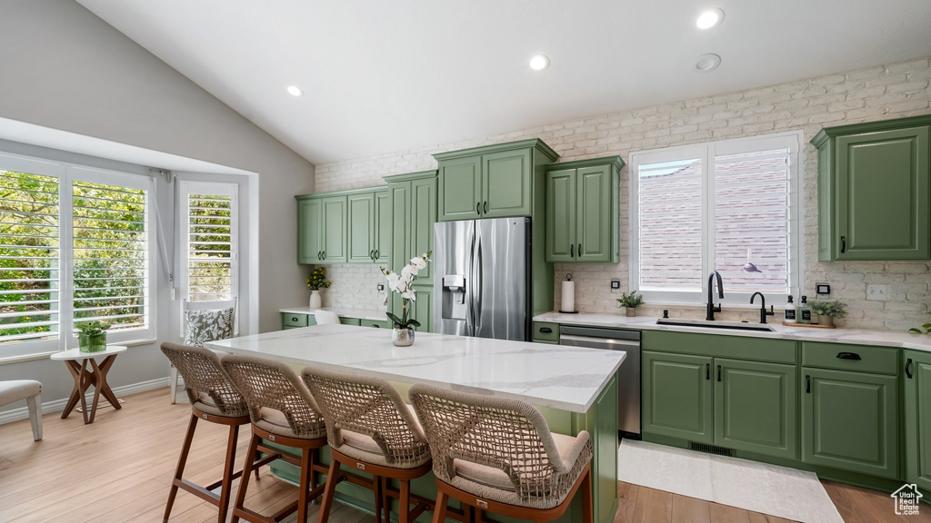 Kitchen featuring appliances with stainless steel finishes, green cabinets, a sink, vaulted ceiling, and recessed lighting