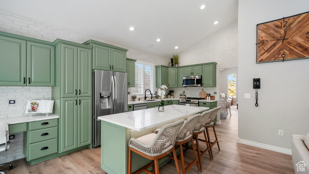 Kitchen with appliances with stainless steel finishes, light wood-style floors, green cabinets, recessed lighting, and high vaulted ceiling
