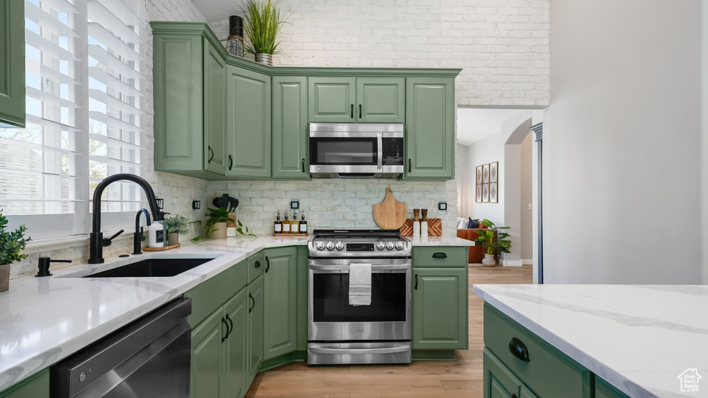 Kitchen with appliances with stainless steel finishes, green cabinets, a sink, light wood finished floors, and backsplash