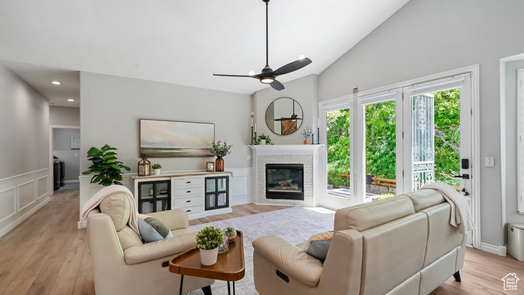 Living area featuring light wood-type flooring, ceiling fan, lofted ceiling, a glass covered fireplace, and wainscoting