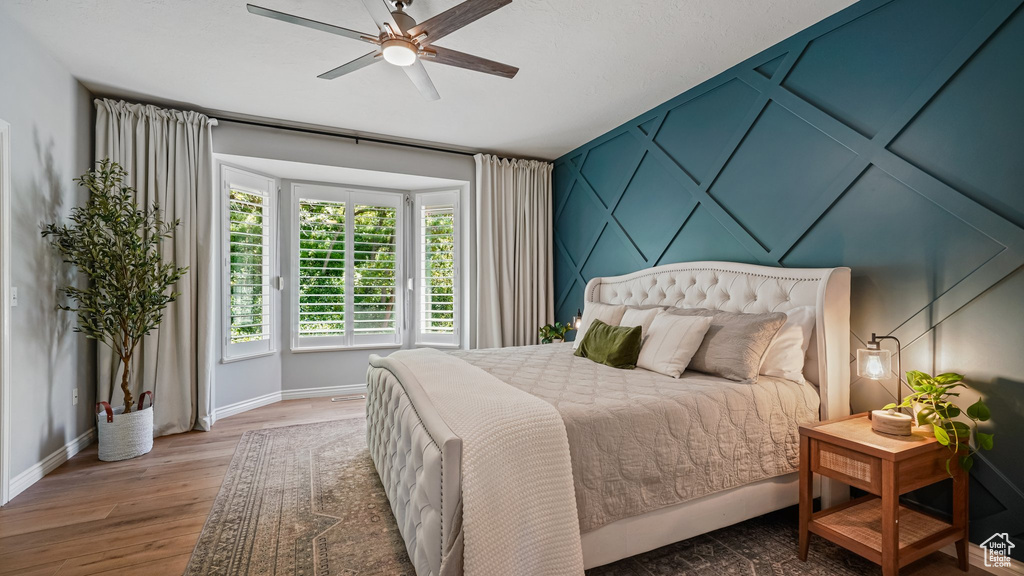 Bedroom featuring baseboards, wood finished floors, a ceiling fan, and a decorative wall