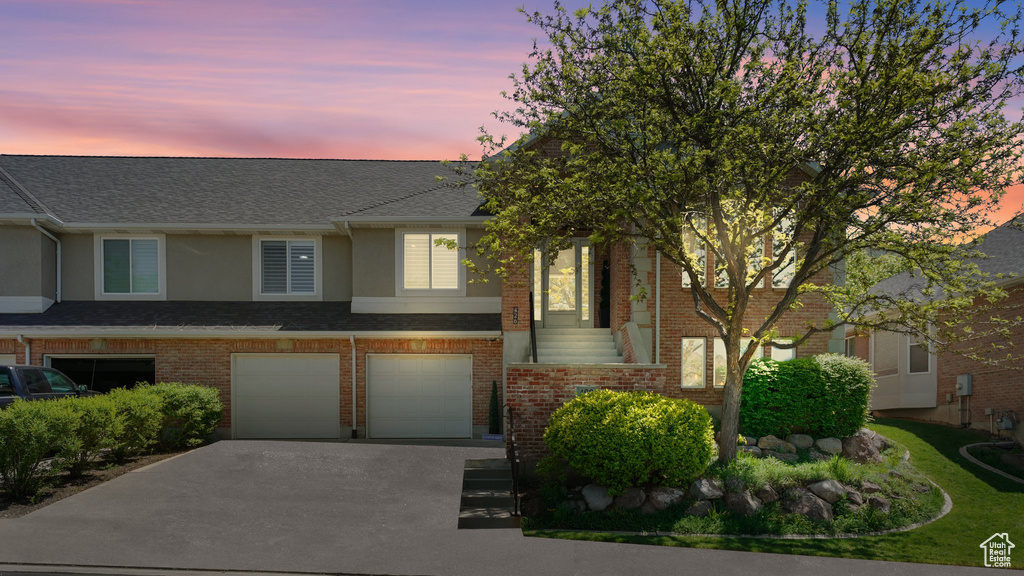 View of property with driveway, a garage, stucco siding, and brick siding