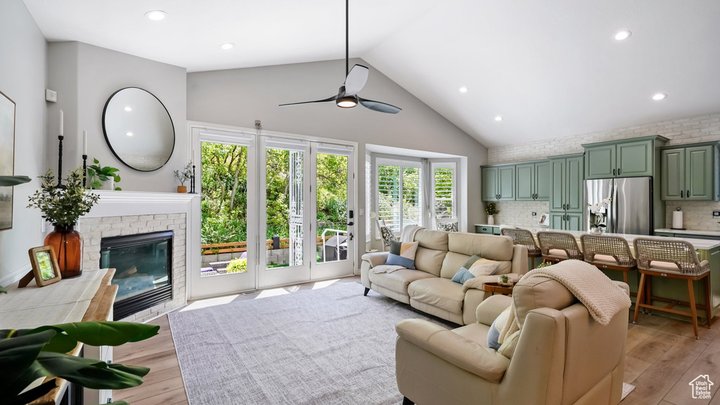 Living room featuring high vaulted ceiling, ceiling fan, light wood finished floors, recessed lighting, and a brick fireplace