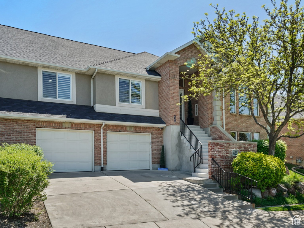 View of property with concrete driveway, stucco siding, an attached garage, stairs, and roof with shingles