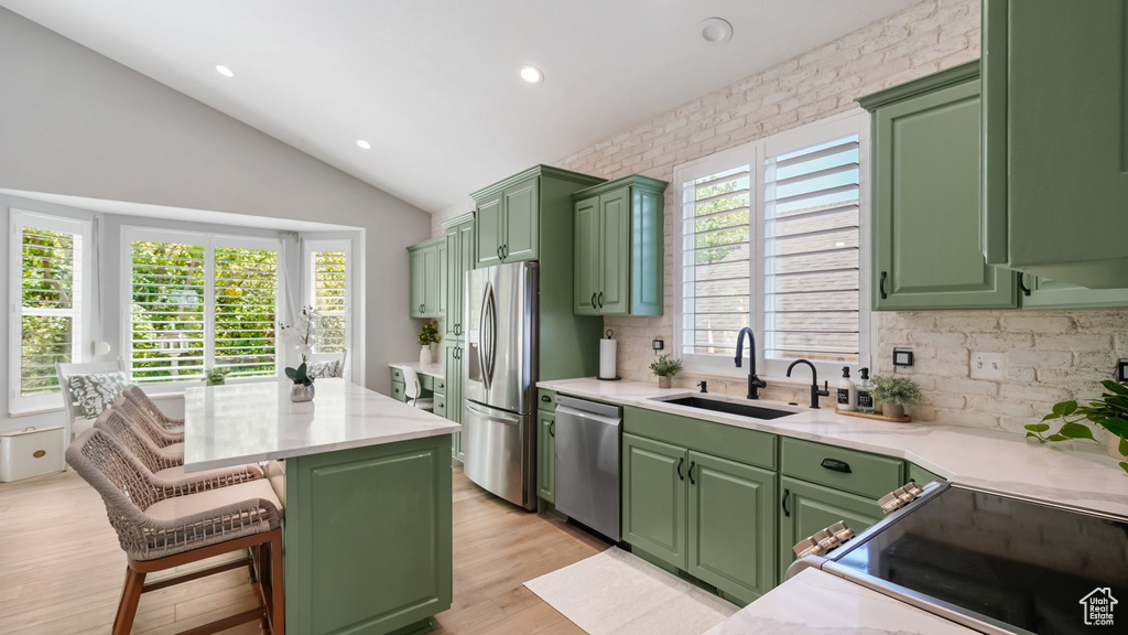 Kitchen featuring a sink, appliances with stainless steel finishes, green cabinetry, tasteful backsplash, and lofted ceiling