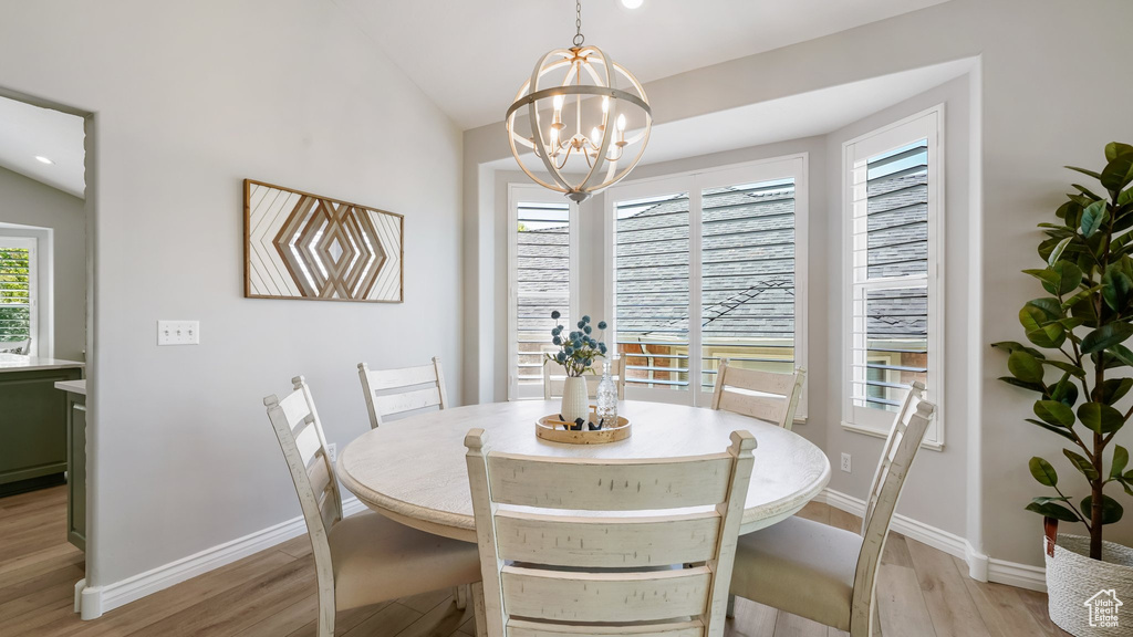Dining room featuring light wood-style flooring, baseboards, a chandelier, and lofted ceiling