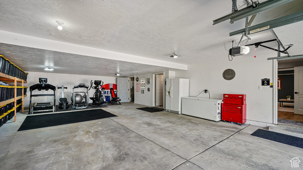 Garage featuring white refrigerator with ice dispenser and a garage door opener